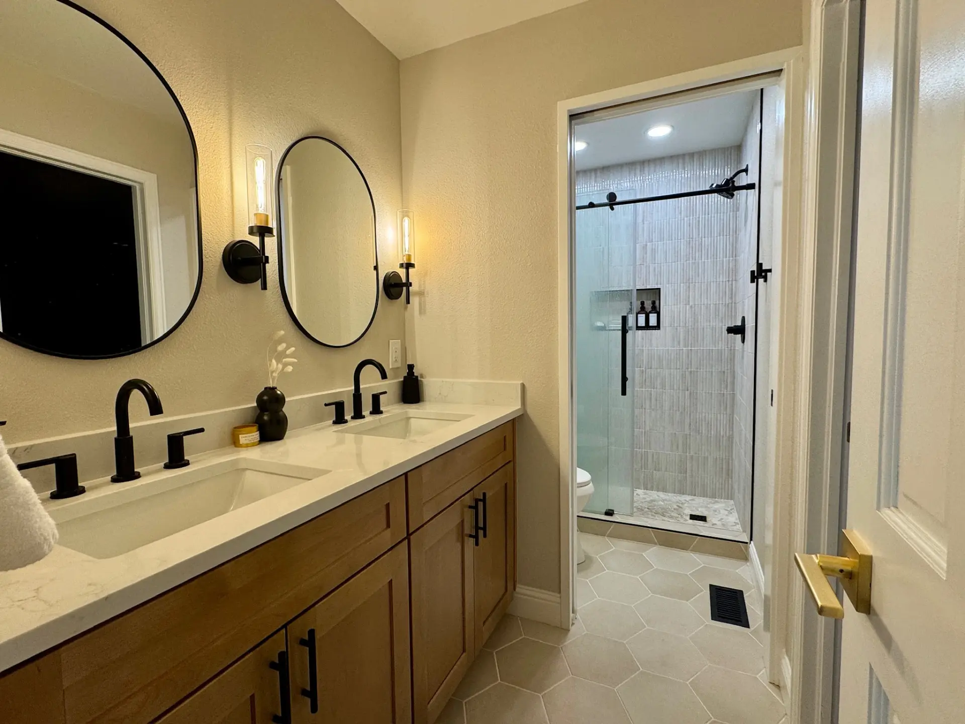 Double vanity with oak cabinets, quartz counters, oval black-framed mirrors, and black fixtures