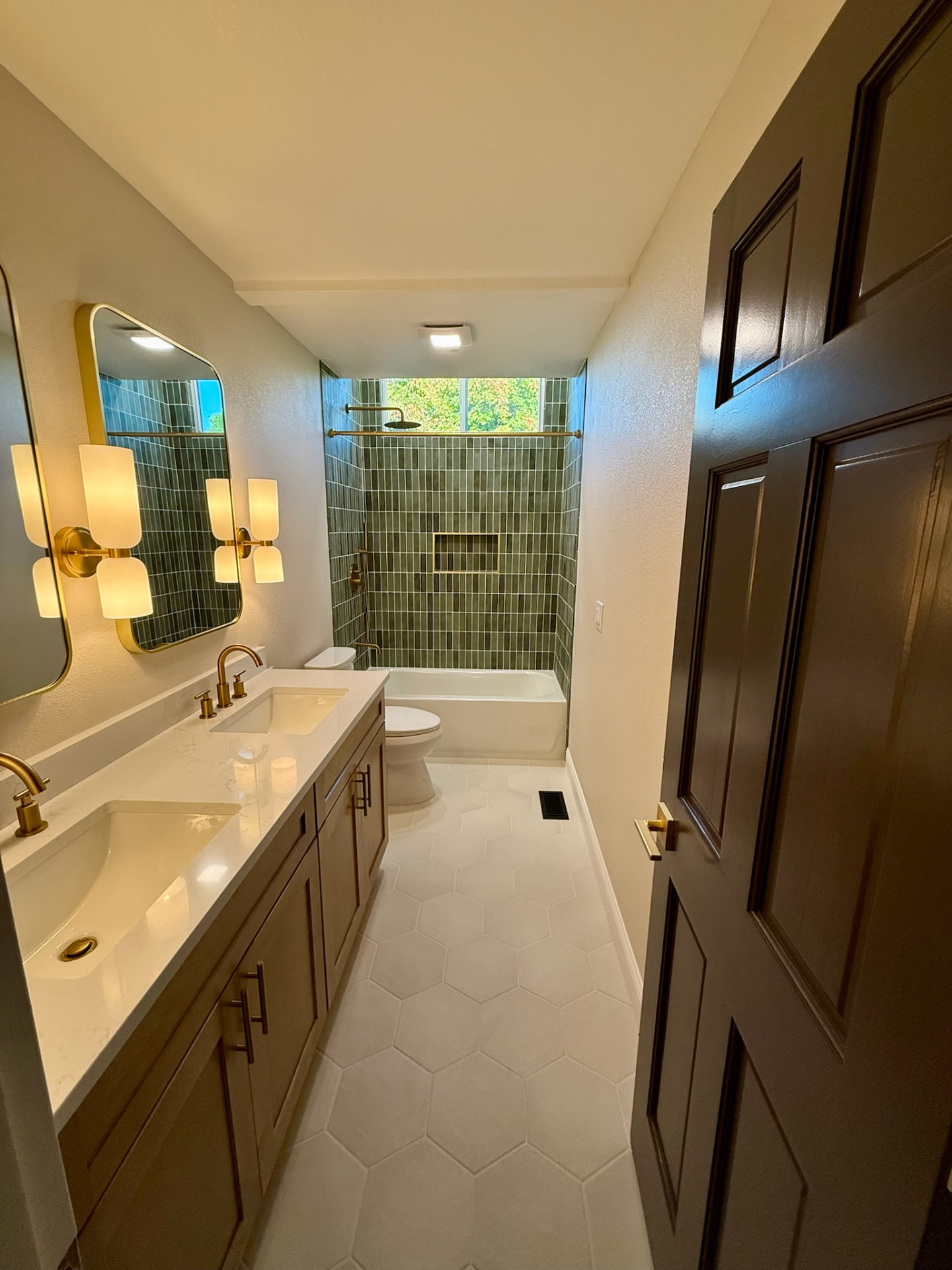 Remodeled bathroom with green tile, brass fixtures, and hexagon tile floor